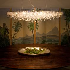 a chandelier hanging over a wooden table in front of a wall with palm trees