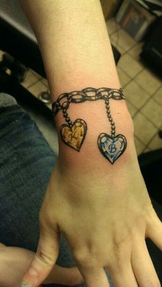 a person's arm with two heart shaped tattoos on it and a chain attached to the wrist