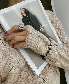 a woman is holding a magazine with her hand on her chest and wearing a ring