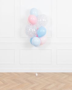 a bunch of balloons floating in the air on top of a wooden floor next to a wall