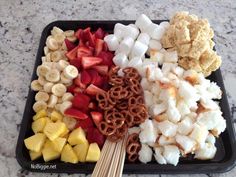 there are many different types of food in the trays on the counter top, including marshmallows, strawberries, and bananas