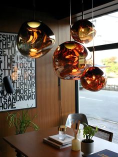 three hanging lights above a wooden table in a room with large windows and artwork on the wall