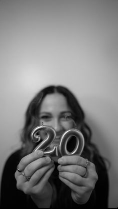 a woman holding up two metal numbers in front of her face