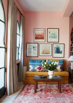 a living room with pink walls and pictures on the wall above the couch, along with a coffee table