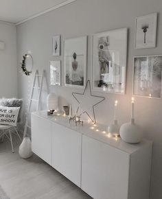 a living room with white furniture and pictures on the wall, candles in front of them