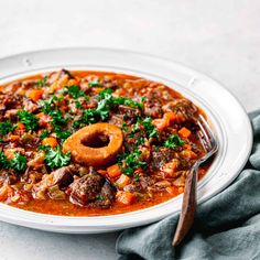 a bowl of stew with meat and vegetables on a white plate next to a wooden spoon