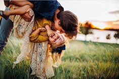 a woman holding a child in her arms while standing on top of a grass covered field