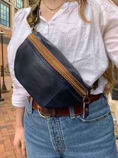 a woman wearing a white shirt and blue jeans is holding a brown leather fanny bag