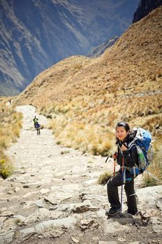 a woman with a backpack and hiking poles on a rocky path in the middle of mountains