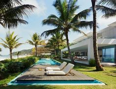 an outdoor pool with lounge chairs and palm trees next to the ocean in front of a house