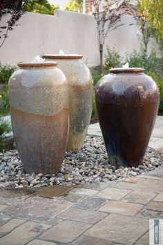 two large vases sitting next to each other on top of a stone floor covered ground