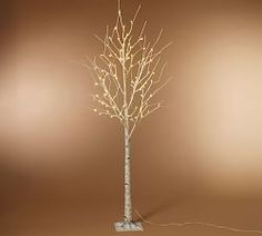 a white tree with lights on it in front of a brown wall and two lamps