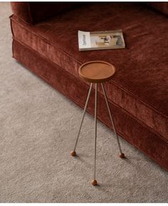 a small wooden table sitting on top of a floor next to a red couch with a magazine