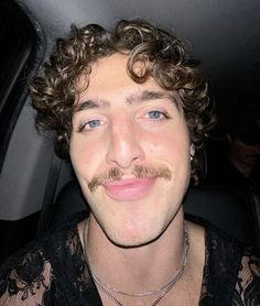 a man with curly hair and a moustache on his face in a car