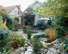 the back yard is full of plants, rocks and water features for an outdoor dining area