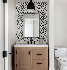 a white toilet sitting next to a bathroom sink under a mirror on top of a wooden cabinet