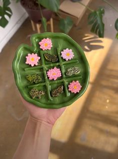 a person holding a green plate with pink flowers on it in front of a potted plant