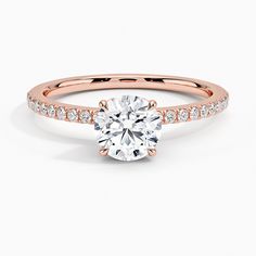 a rose gold engagement ring with diamonds on the band and a round cut diamond in the center