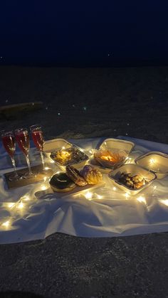 a table with food and wine glasses on it at night in the desert, lit up by fairy lights