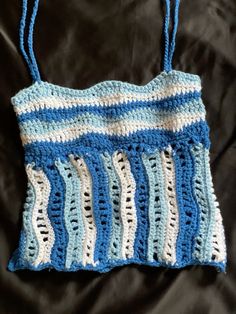 a crocheted blue and white purse sitting on top of a black cloth covered bed