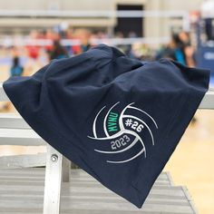 a towel sitting on top of a wooden bench in front of a volleyball court with people standing around