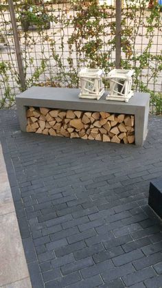 a bench sitting next to a pile of firewood on top of a brick sidewalk