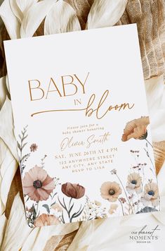 a baby in bloom card with flowers and leaves on it's back, next to some feathers