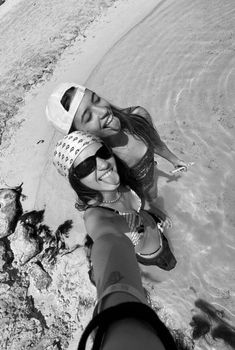 two girls are standing in the water at the beach and one is holding her arm around the other's neck