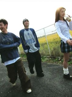 three young people standing next to each other in front of a fence and grass field