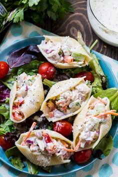 a blue plate topped with pasta shells and salad next to a bowl of ranch dressing