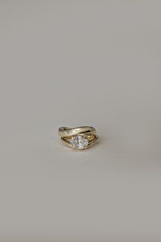 a gold ring with two diamonds in it on a gray background, the middle one has a curved band