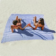 two women in bikinis laying on a towel at the beach