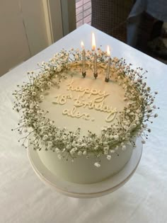 a birthday cake with white frosting and lit candles on it sitting on a table