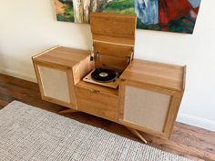 a record player sitting on top of a wooden cabinet next to a rug and painting