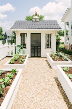 a small white house with lots of plants in the front and side garden beds around it