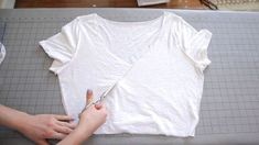 someone cutting up a t - shirt with scissors on top of a piece of paper