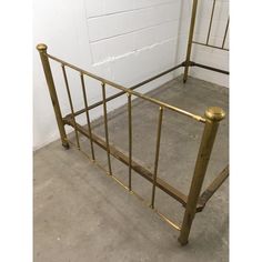 a metal bed frame with gold colored rails and foot board on concrete floor next to white brick wall