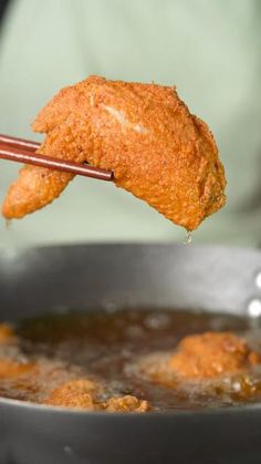 a fried chicken wing being dipped with chopsticks in a frying pan filled with broth