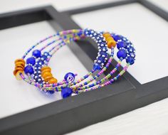 This beaded wrap bracelet is made with four rows of beads strung onto silver plated memory wire. Coordinating glass seed beads are paired with various glass, crystal and shell beads in shades of cobalt blue and golden yellow with accents of silver throughout. Super bold and colorful, this bracelet will be a pretty splash of color to any outfit! Memory wire maintains its shape, no matter how it is twisted or stretched. Instead of using a clasp, you wind it onto your wrist, making it easy to fit a Blue Wrap Bracelet With Spacer Beads, Blue Wrap Bracelet With Colorful Beads For Gifts, Blue Wrap Bracelet With Colorful Beads As Gift, Blue Spacer Beads Bracelets For Festivals, Blue Festival Bracelets With Spacer Beads, Hand Wrapped Blue Beaded Bangle Bracelet, Blue Wrap Bracelet With Colorful Beads For Festivals, Festival Wrap Bracelet With Colorful Beads, Festival Blue Wrap Bracelet With Colorful Beads