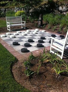 a checkerboard chess board in the middle of a garden with two white benches