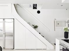 a kitchen with white walls and flooring next to a stair case in front of a refrigerator