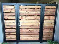 a wooden gate with metal bars on the sides and green plants in pots behind it