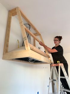 a woman standing on a ladder working on a piece of wood that is attached to the ceiling