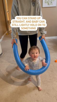 a woman standing next to a toddler holding a blue ring in her hands with the caption you can stand up straight, and baby can still be seen on it't