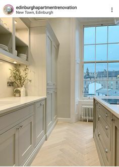 a large kitchen with white cabinets and wood flooring next to a window overlooking the city