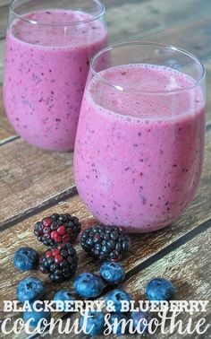 two glasses filled with berry smoothie on top of a wooden table next to berries