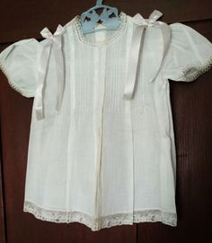 An adorable unworn baby dress from the later 1930s or 1940s. The dress is made in a soft batiste white cotton. The yoke is made of four rows of pin tucks, in a series of four, on the front dress yoke. Each set is separated with a row of feather stitch embroidery.  Narrow lace trim edges the neck line and short puff sleeves.  A wider Alencon lace edges the hem.  Two acetate ribbon bows, with streamers, are attached at the shoulders.  The back of the dress is made on a plain yoke with two buttons fastening the closing. No labels to indicate the origin nor any size tags.  It would probably fit a child about 4 to 6 months of age.  Measurements:  15-1/4" long from the neck line to hem.  9-1/2" across from shoulder to shoulder.  23" around the chest.   Condition:  Unworn and never laundered.  Yo Classic White Vintage Dress With Short Sleeves, Cotton Baptism Dress With Short Sleeves For Daywear, Cotton Short Sleeve Baptism Dress, Classic Short Sleeve Cotton Baptism Dress, White Cotton Vintage Dress With Short Sleeves, Cotton Baptism Dress With Short Sleeves, White Short Sleeve Baptism Dress For Daywear, White Vintage Baptism Dress For Daywear, White Baptism Dress With Short Sleeves For Daywear