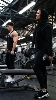 two people in a gym with dumbbells and one person wearing a hoodie