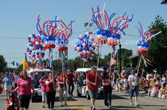 some people are walking down the street with balloons and streamers in the shape of american flags