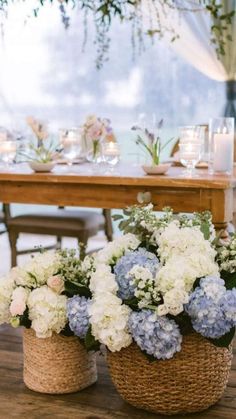 two baskets filled with blue and white flowers on top of a wooden table under a chandelier